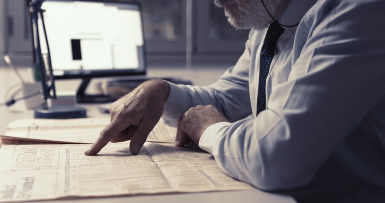 Businessman pointing at a newspaper with a screen in the background